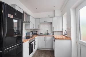 a kitchen with white cabinets and a black refrigerator at Haw Hill House - modern 4 bed in Normanton