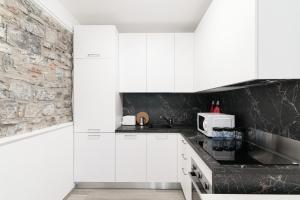 a kitchen with white cabinets and a stone wall at Olimpia Via Vitani - The House Of Travelers in Como
