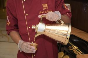 a man in a red shirt holding a copper pot at Areen Hotel Airport in Jeddah