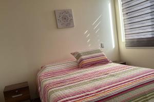 a bedroom with a bed with a striped blanket and a window at Condo en La serena in La Serena
