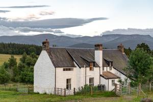 an old white house with mountains in the background at Achnahatnich House in Aviemore