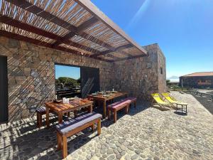 a patio with benches and tables and a stone wall at Vila Babosa in Porto Novo