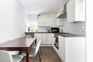 cocina con armarios blancos y mesa de madera en Gorgeous London Town House Sleeps up to 8 en Londres