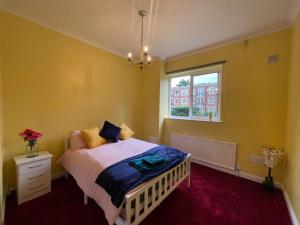 a bedroom with a bed with yellow walls and a window at Elegant Weybridge Apartment near Train Station in Oatlands Park