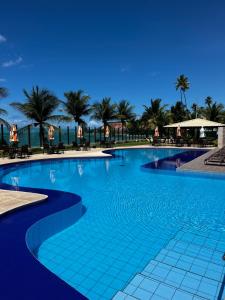 uma grande piscina azul com palmeiras ao fundo em Cobertura e Flat Tabatinga em Conde