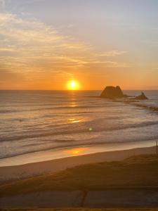 - un coucher de soleil sur la plage avec l'océan et les rochers dans l'établissement Harmony at the Heads, à Mangawhai