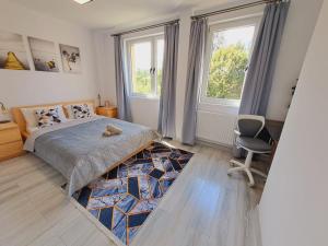 a bedroom with a bed and a chair and two windows at Limanowa Sunriser Apartment in Limanowa
