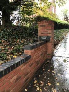 a brick wall with a sign on it next to a sidewalk at Hillfields Farm Barn - A Rural Equestrian Escape in Coventry