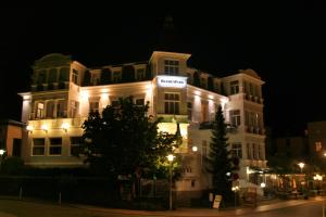 Un grand bâtiment blanc avec des lumières allumées la nuit dans l'établissement Hotel Buchenpark, à Bansin