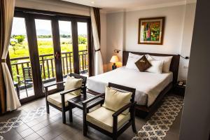 a bedroom with a bed and two chairs and a balcony at Hoi An Odyssey Hotel & Spa in Hoi An