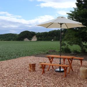 a picnic table and an umbrella in front of a field at fukiconoie in Tokachi