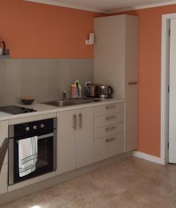 a kitchen with white cabinets and an orange wall at Bunny Cottage in Masterton