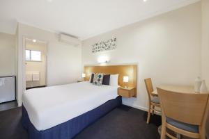 Una habitación de hotel con una gran cama blanca y un escritorio. en Hamilton Townhouse Motel, en Hamilton