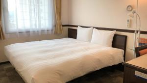 uma cama com lençóis brancos e almofadas num quarto em Toyoko Inn Ise Matsusaka Ekimae em Matsuzaka