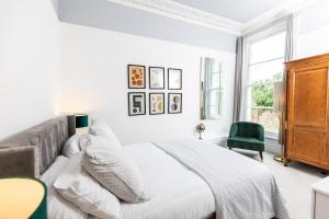 a white bedroom with a bed and a green chair at 10 Sydenham - By Luxury Apartments in Cheltenham