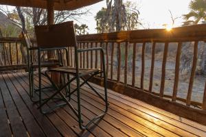 Nata Lodge في Nata: كرسي جالس على سطح خشبي مع غروب الشمس