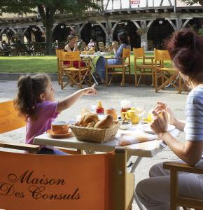 Eine Frau und ein kleines Mädchen sitzen an einem Tisch mit Essen in der Unterkunft La Maison des Consuls in Mirepoix