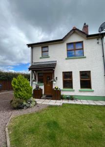 a white house with a brown door and a yard at Whitepark Cottage - your home away from home in Ballycastle