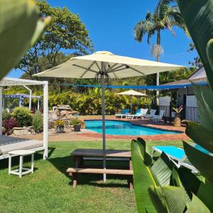 un patio con sombrilla, banco y piscina en The Carmel Yamba en Yamba