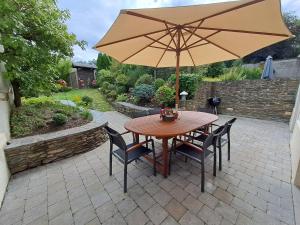 une table en bois avec des chaises et un parasol dans l'établissement Gîte L'Hôte-Antique, à Bouillon