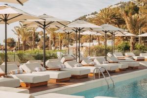 Eine Reihe von Liegestühlen und Sonnenschirmen neben einem Pool in der Unterkunft Hotel Riomar Ibiza, a Tribute Portfolio Hotel in Santa Eulària des Riu