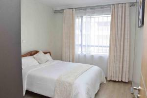 a bedroom with a white bed and a window at Blissful Airport Serviced Apt. in Nairobi