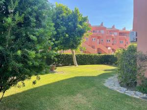 einen grünen Hof mit einem Baum und einem rosa Gebäude in der Unterkunft Manilva Beach: Your Costa del Sol Getaway! in Castillo de Sabinillas