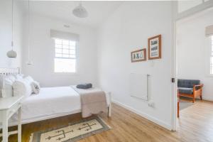 a white bedroom with a bed and a mirror at Sunny Windsor Apartment in Kalk Bay in Cape Town