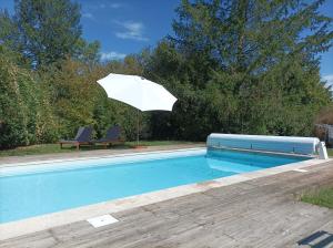 a swimming pool with an umbrella and two chairs and a table at Longère avec piscine in Couffy
