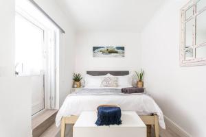 a white bedroom with a large bed with a blue seat at Dalebrook Cottage in the heart of Kalk Bay in Cape Town