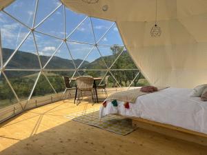 a bedroom with a bed and a table in a room with large windows at Tranquil Dome - Manta's Retreat Glamping Cornereva in Cornereva
