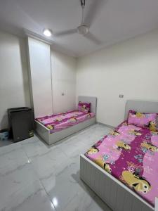 two beds in a white room with purple sheets at Moon light Hotel in Kafr Mas‘ūd