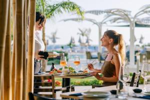 two women sitting at a table eating food and drinking wine at Ivi Mare - Designed for Adults by Louis Hotels in Paphos