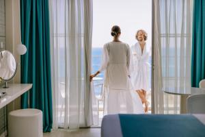 a woman in a white dress standing next to a window at Ivi Mare - Designed for Adults by Louis Hotels in Paphos