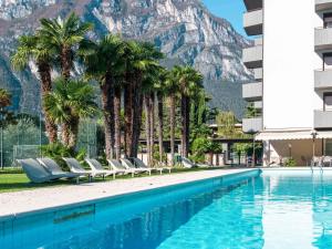 a pool with palm trees and a mountain in the background at Apartment Comfort by Interhome in Riva del Garda