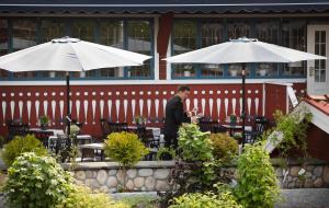 Ein Mann steht vor einem Restaurant mit Tischen und Sonnenschirmen. in der Unterkunft Åkerblads Hotell Gästgiveri Spa in Tällberg