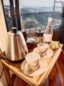 einen Holztisch mit Geschirr, einen Wasserkocher und ein Fenster in der Unterkunft Atardeceres del Cafe in Manizales