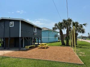 a playground in front of a house with a picnic table at Cast a Waves - Cute Beach Bungalow - Ocean Views - Walk to the Beach in Galveston
