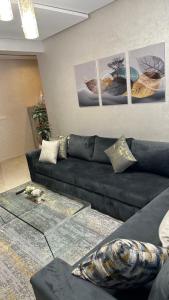 ein Wohnzimmer mit einem schwarzen Sofa und Bildern an der Wand in der Unterkunft Haut Standing Appartement - Centre Ville Oujda in Oujda