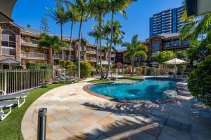 a swimming pool with palm trees and a building at Oceanside Cove in Gold Coast