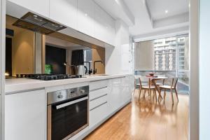 a kitchen with white cabinets and a table with chairs at 'Collins Central' Sleek Light-filled Pad in the CBD in Melbourne
