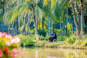 due persone sedute su una panchina accanto a un corpo d'acqua di Armin Homes Ecopark Red Riverview Sky Oasis a Kim Quan