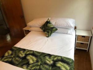 een bed met witte lakens en kussens met een groen bladpatroon bij Are Ara - House of Pineapple in Titikaweka