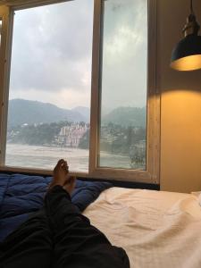 a person laying on a bed looking out a window at Joey's By The Ganges in Rishīkesh