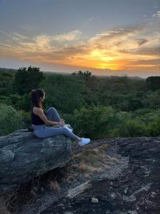 Big Game - Udawalawe by Eco Team في اوداوالاوي: امرأة جالسة على صخرة تشاهد غروب الشمس