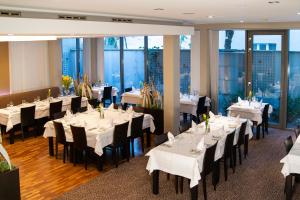 a restaurant with white tables and black chairs and windows at Hotel Avance in Bratislava