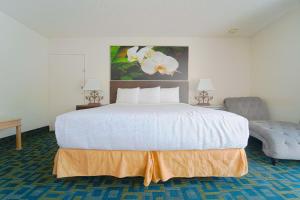 a bedroom with a large white bed and a chair at Royal Plaza Inn in Indio