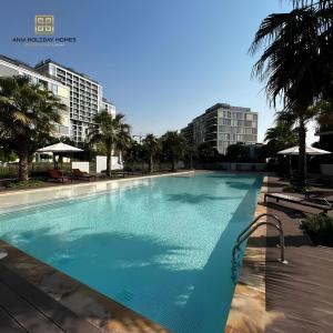 a large blue swimming pool with palm trees and buildings at ANW Vacation Homes - One bedroom apartment Afnan 4 Midtown Dubai Production City in Dubai