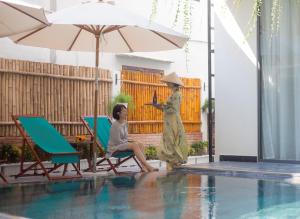 two women sitting next to a pool with an umbrella at MaiChi Villa Hoi An in Hoi An