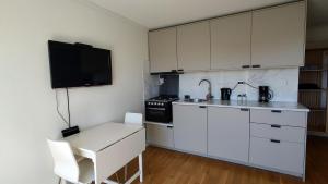 a kitchen with white cabinets and a table and a tv at Kaldvell Apartman in Lillesand